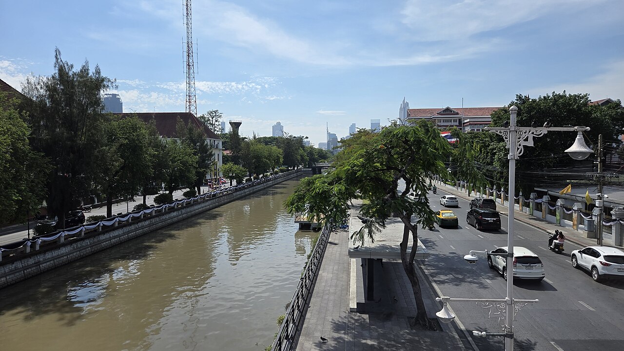 曼谷一条城市运河的资料照片,运河旁有道路、树木和建筑,远处可见市中心天际线。