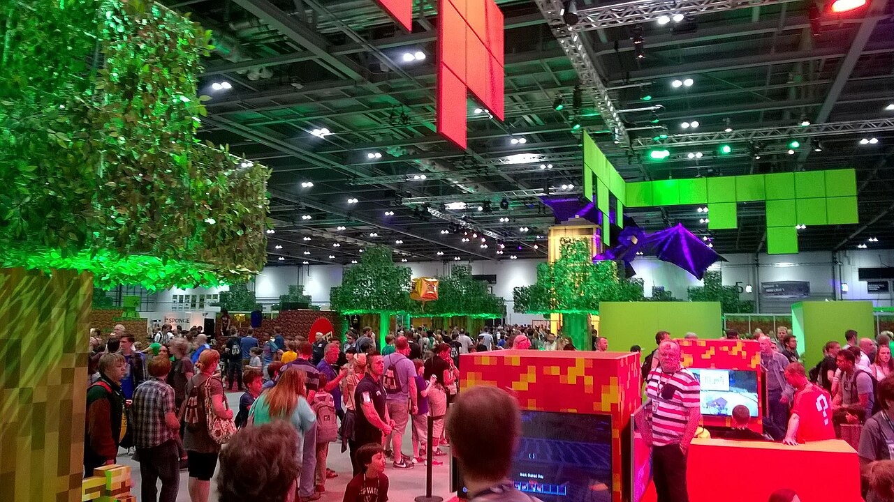 资料照片:拥挤的 MineCon 2015 展厅内有《我的世界》方块主题展台、大型末影龙模型和参观者。