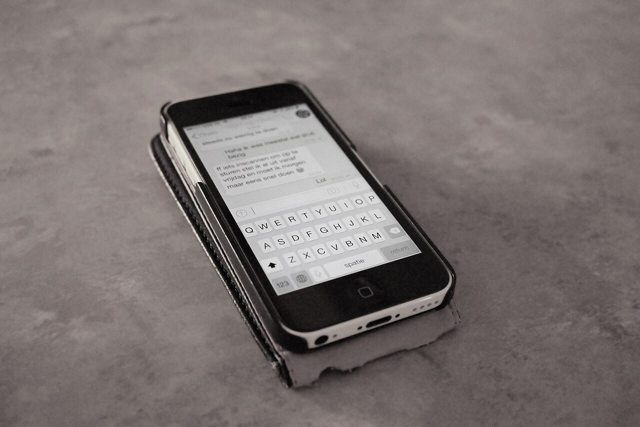Foto de archivo de un teléfono inteligente negro sobre una mesa con una conversación de mensajes y teclado en pantalla.