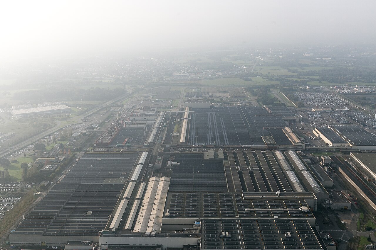 Archive aerial view of the PSA Rennes manufacturing complex in France, showing large factory halls, parking areas, roads and surrounding landscape.
