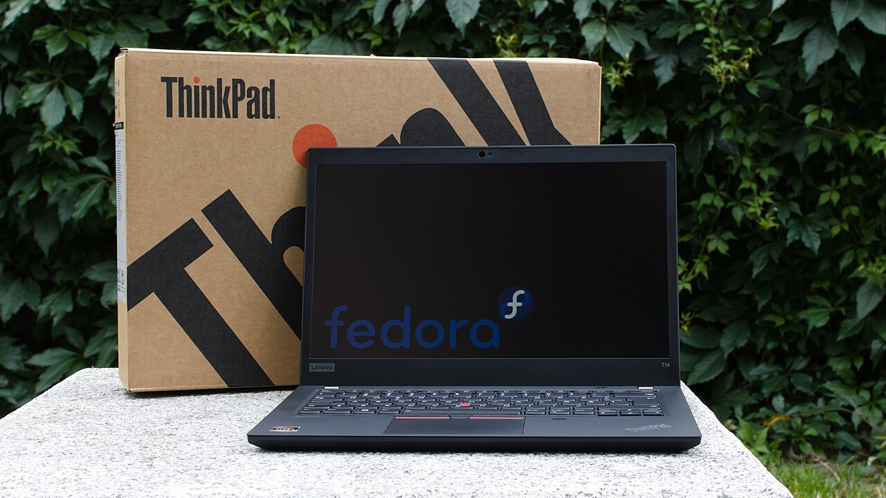 资料照片:一台黑色 Lenovo ThinkPad T14 打开摆在桌面上,后方可见包装。