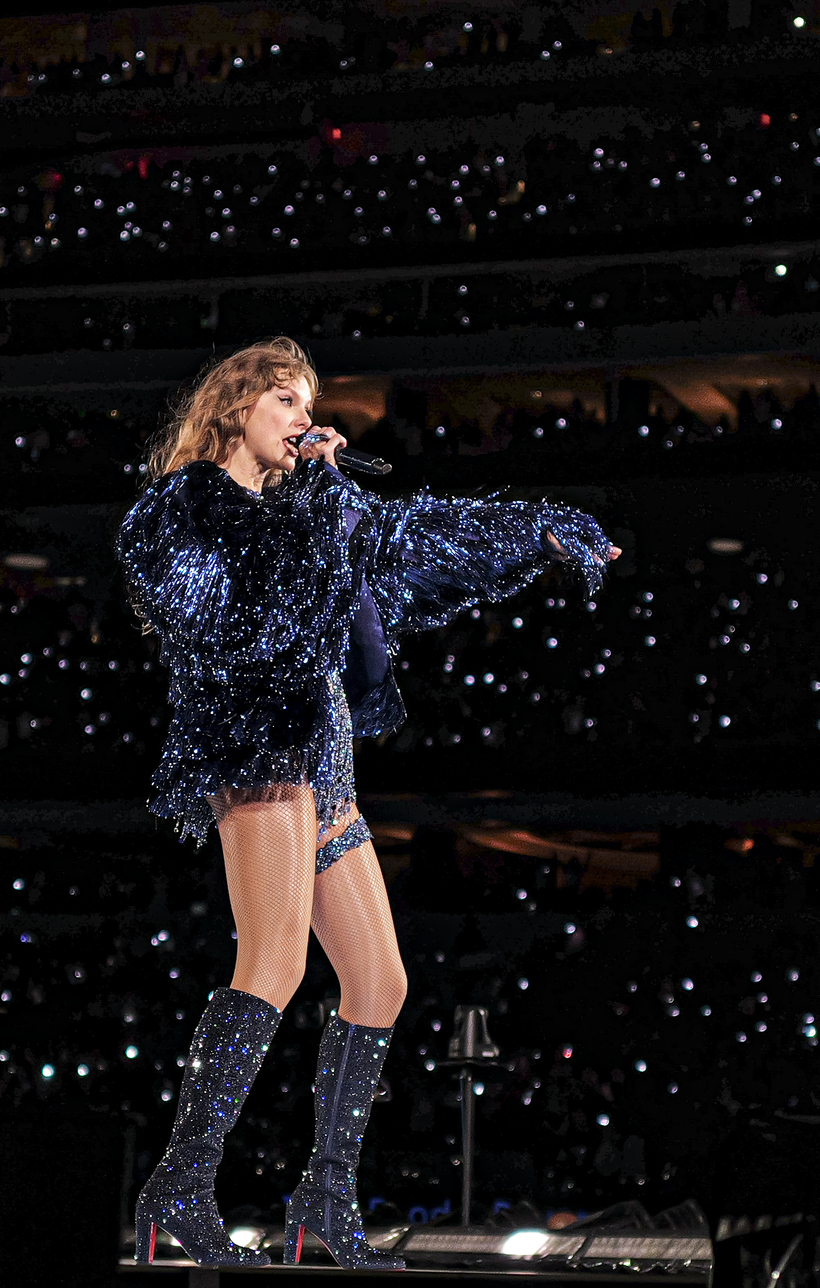 资料照片:Taylor Swift于2023年在SoFi Stadium的Eras Tour舞台上演唱,身穿深色亮片服装并手持麦克风。